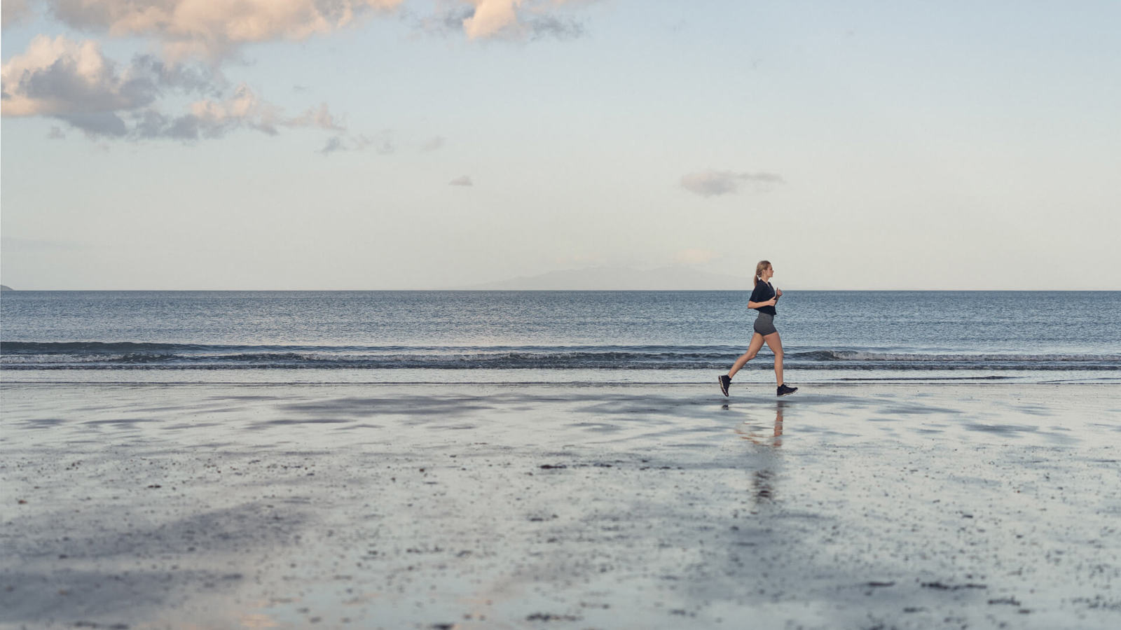young lady running at the beach - side view