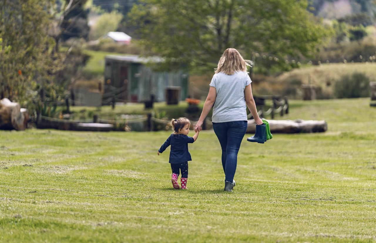 young mum and daughter walking in the park - back view