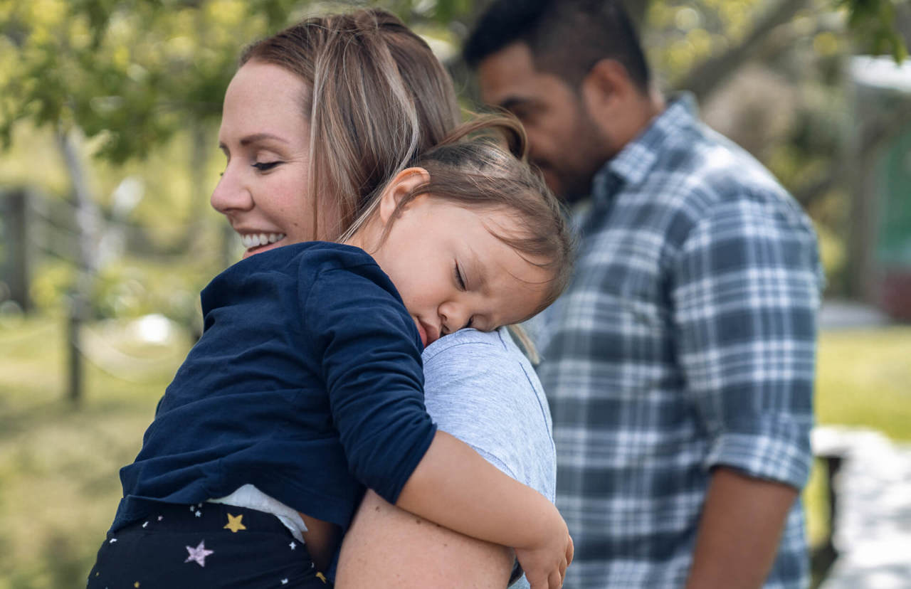 baby girl sleeping on mum's shoulder - father in the background